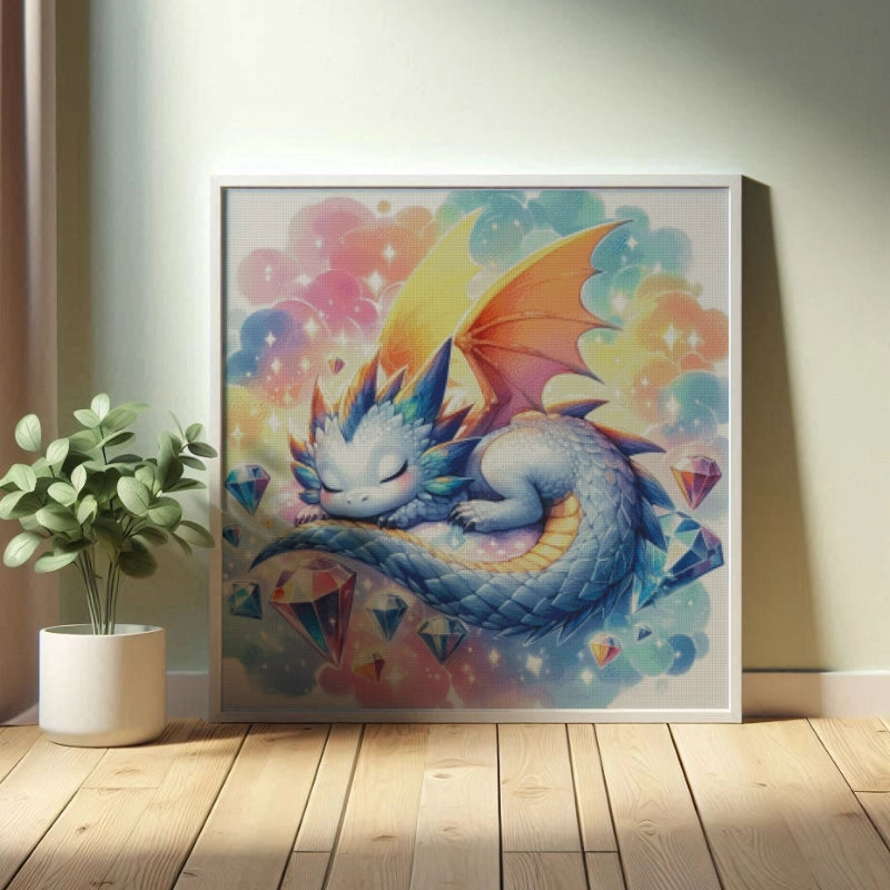 Ein weißer Rahmen steht vor einer Wand. Mit einer verpixelten Vorschau für das Bild, wie es aussehen würde, wenn es mit den Steinen gelegt wurde. Ein kleiner schlafender Drache mit bläulich hellen Schuppen liegt schlafend herum. Seine Flügel sind orangefarben, seine Wangen sind rosa. Sein langer Schwanz liegt eng an ihm, so dass seine Vorderpfoten diesen berühren. Um ihn herum sind glitzernde Diamanten. Der Hintergrund ist wolkig in bunten pastelligen Farben.